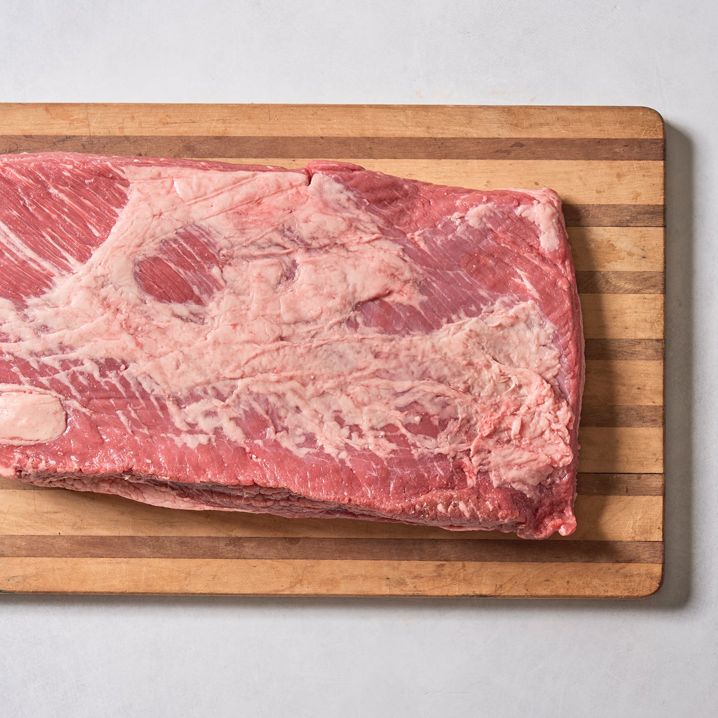 A large, raw Ninth & Prime Brisket with marbled fat rests on a wooden cutting board against a light background.