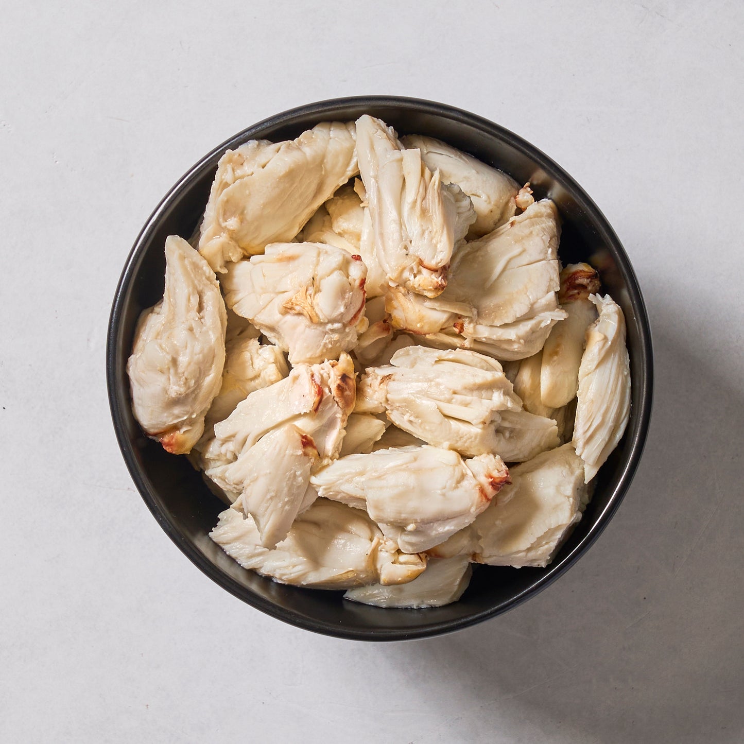 A black bowl filled with Ninth & Prime Colossal Crab Meat—premium blue swimming crab with large white chunks—sits on a light-colored surface.