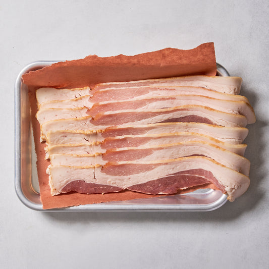 Several strips of Ninth & Prime Millionaire Thick Cut Bacon are neatly arranged on a metal tray lined with brown parchment paper, set against a light-colored background.