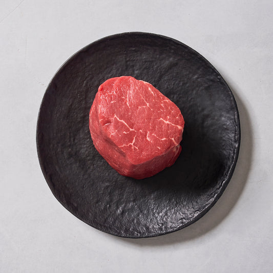 A raw Ninth & Prime Center-Cut Filet Mignon, famed as the king of steaks, rests on a textured black plate against a light gray background.