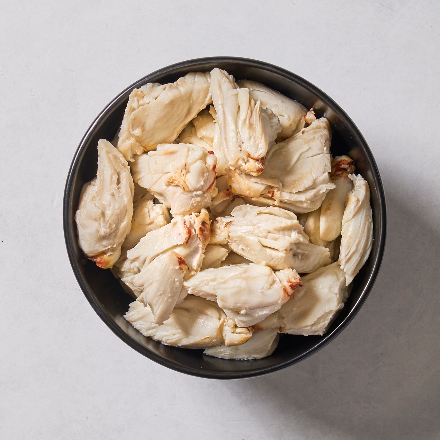 A black bowl filled with Ninth & Prime Colossal Crab Meat—premium blue swimming crab with large white chunks—sits on a light-colored surface.