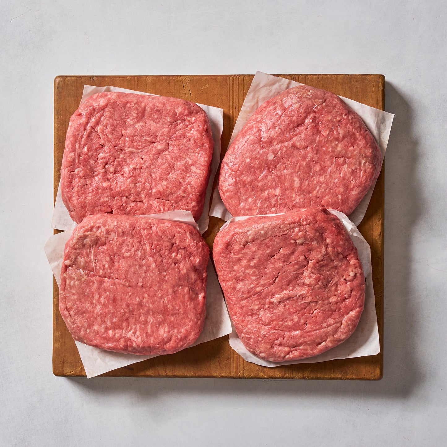 Ninth & Prime Wagyu Beef Burgers—four gourmet raw patties on parchment squares, arranged on a wooden board—are perfect for creating restaurant-quality burgers at home.