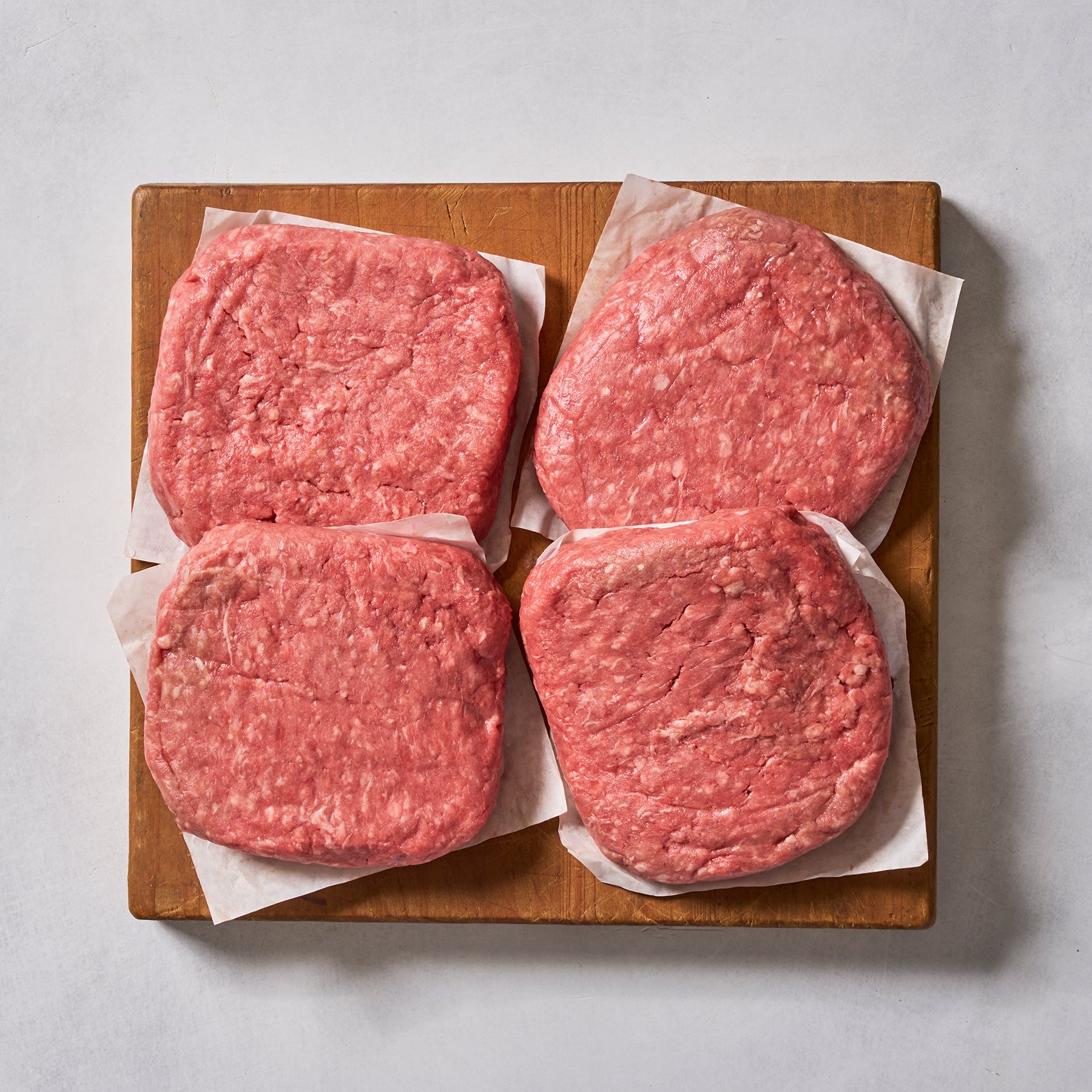 Ninth & Prime Wagyu Beef Burgers—four gourmet raw patties on parchment squares, arranged on a wooden board—are perfect for creating restaurant-quality burgers at home.