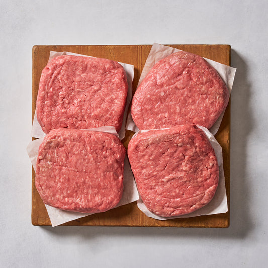 Ninth & Prime Wagyu Beef Burgers—four gourmet raw patties on parchment squares, arranged on a wooden board—are perfect for creating restaurant-quality burgers at home.